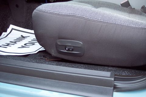 2001 Ford Crown Victoria - Close-up of the driver's seat controls, including lumbar adjustment, with a 'Thank You' sign on the floor.