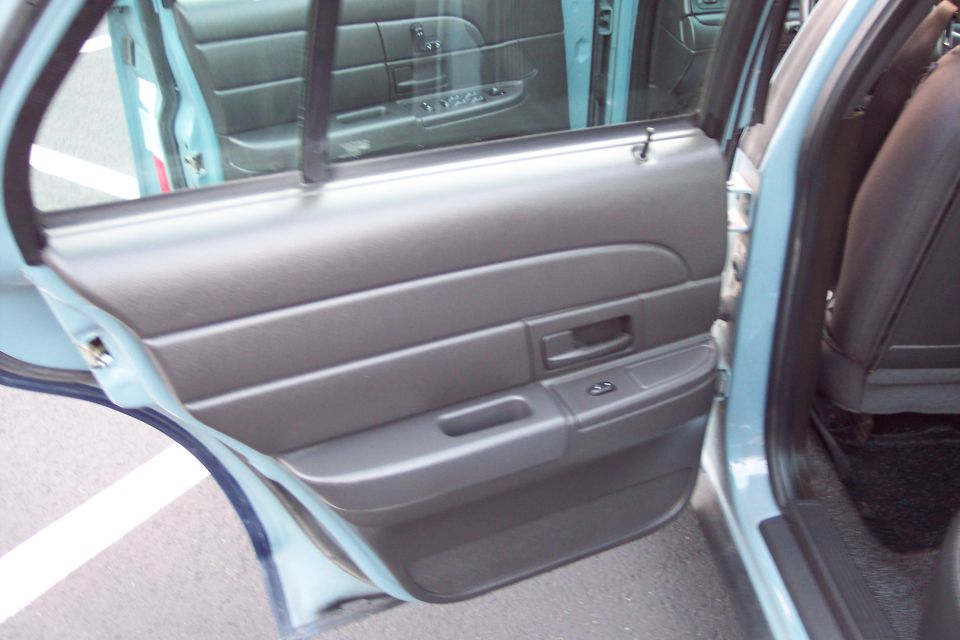Interior shot of a car's rear passenger door panel and seat. The door panel is dark gray with horizontal ridges and a black handle. The seat is black leather