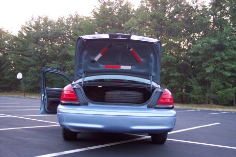2001 Ford Crown Victoria - The rear of a blue sedan is shown with the trunk open, revealing a spare tire and the interior of the car.