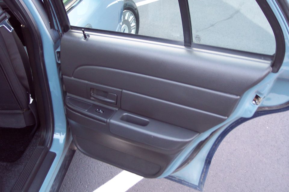 Interior door panel of a 2001 Ford Crown Victoria, light blue exterior, black interior trim, showing window controls and door handle