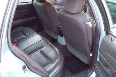 2001 Ford Crown Victoria - The interior of a 2001 Ford Crown Victoria shows the rear seating area with black leather upholstery and light blue exterior paint visible.