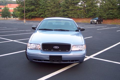 2001 Ford Crown Victoria - A light blue Ford Crown Victoria is parked in a lot with a black pickup truck in the distance.
