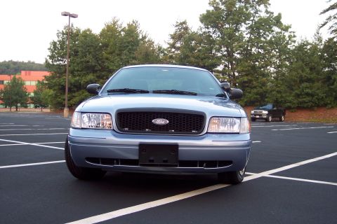 2001 Ford Crown Victoria - A blue 2001 Ford Crown Victoria is parked in a lot, with a black pickup truck visible in the distance.