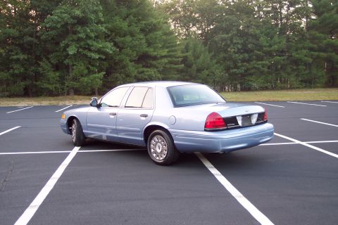 2001 Ford Crown Victoria - A light blue 2001 Ford Crown Victoria is parked in an empty lot, viewed from the rear three-quarter angle.