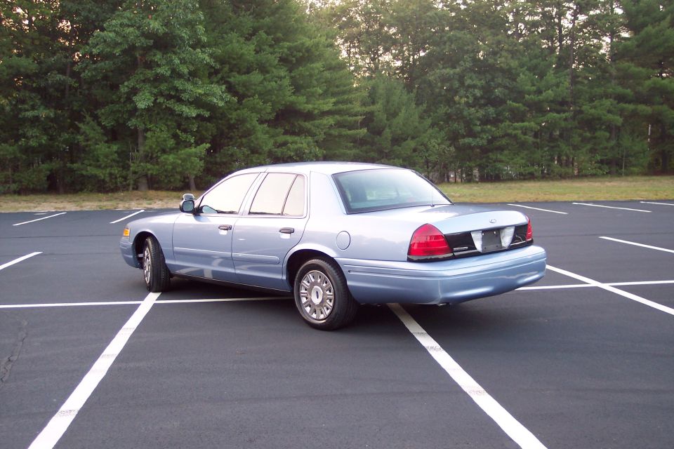 Light blue 2001 Ford Crown Victoria, rear 3/4 view in empty parking lot