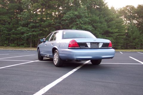 2001 Ford Crown Victoria - Rear view of a light blue 2001 Ford Crown Victoria sedan in an empty parking lot.
