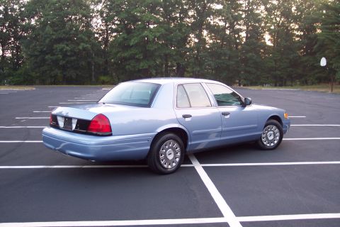 2001 Ford Crown Victoria - Light blue 2001 Ford Crown Victoria parked in an empty lot with trees in the background.