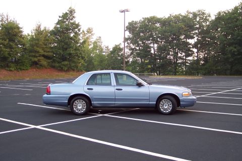 2001 Ford Crown Victoria - A light blue 2001 Ford Crown Victoria is parked in a lot with white lines.