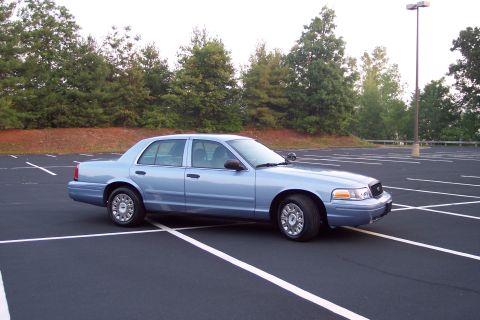 2001 Ford Crown Victoria - A light blue 2001 Ford Crown Victoria is parked in an empty asphalt lot with white parking lines.