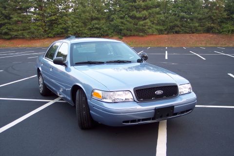 2001 Ford Crown Victoria - A light blue sedan is parked in a lot with trees in the background.