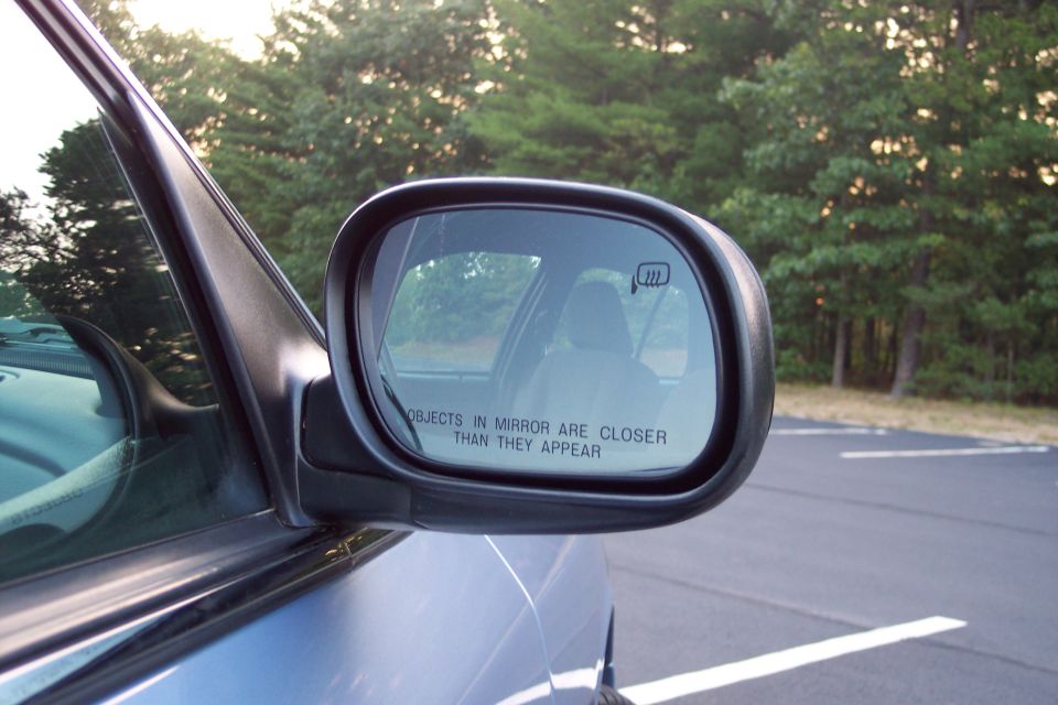 Side mirror of a car showing reflection of interior and trees outside