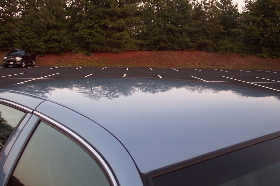 Blue sedan roof and side window in foreground, black pickup truck in background parking lot