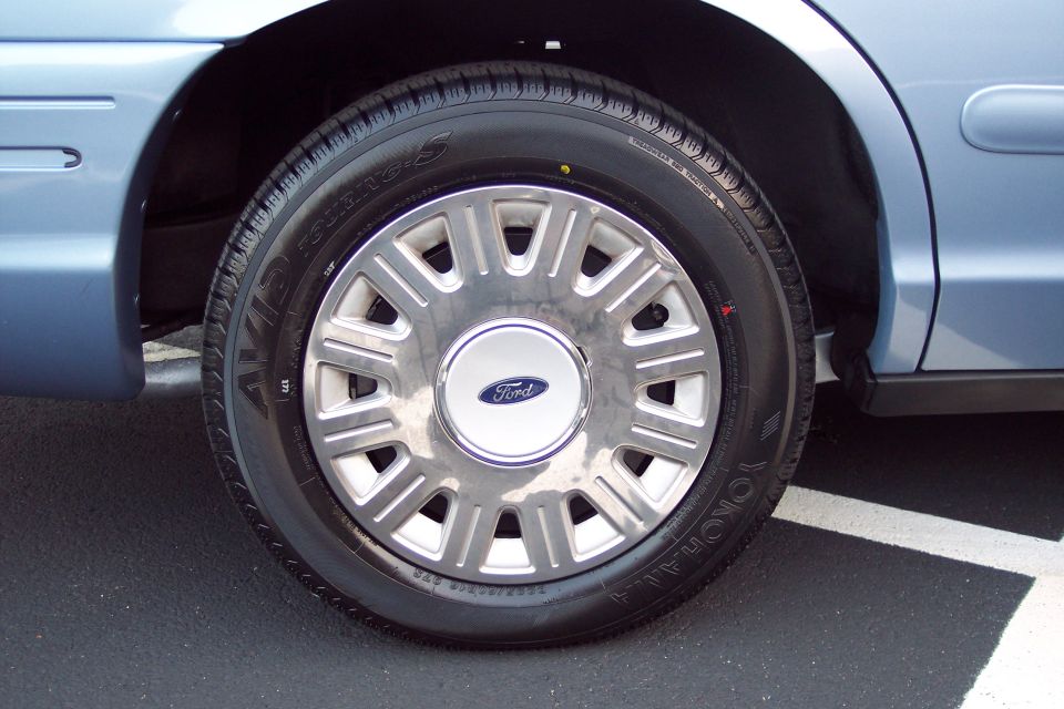 Close-up of a 2001 Ford Crown Victoria's front passenger side wheel and fender. The wheel has a Ford logo