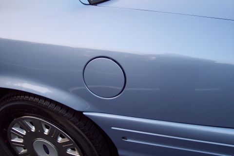 2001 Ford Crown Victoria - Close-up of the rear quarter panel of a light blue sedan, showing the fuel door and wheel well.