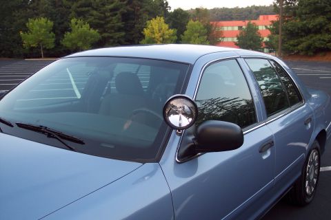 2001 Ford Crown Victoria - A blue 2001 Ford Crown Victoria police car is seen from a three-quarter front view, equipped with a spotlight mounted on the driver's side.
