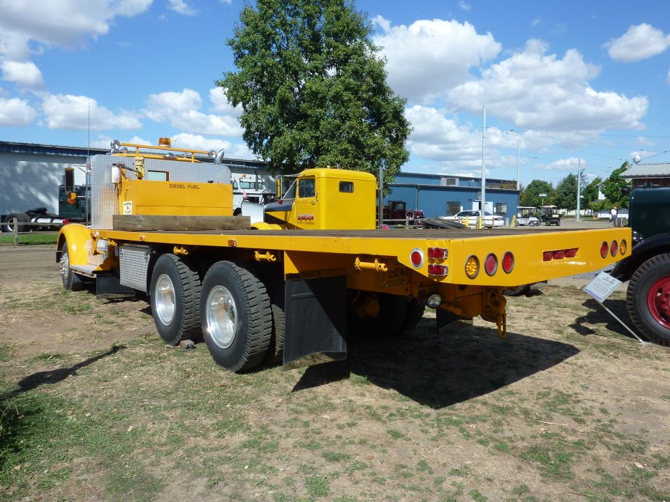Yellow tandem-axle flatbed truck with diesel fuel tank, rear three-quarter view outdoors.