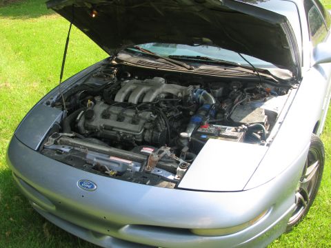 1994 Ford Probe - The engine bay of a silver 1994 Ford Probe is visible with the hood raised, parked on grass.
