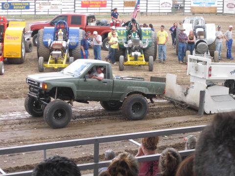 1989 Ford Bronco - A modified pickup truck competes in a pull event, with spectators watching from the stands.