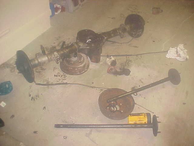 Disassembled rear axle, brake drums, and driveshaft laid out on the floor