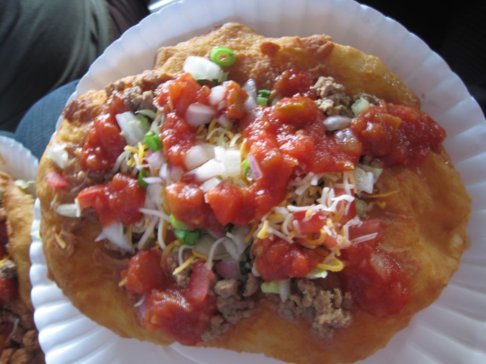Navajo taco with ground beef, cheese, lettuce, salsa, and green onions on a fried dough base