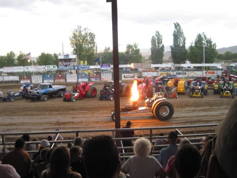 1989 Ford Bronco - Multiple tractor pull vehicles are lined up on a dirt track, with one emitting a large flame from its engine.