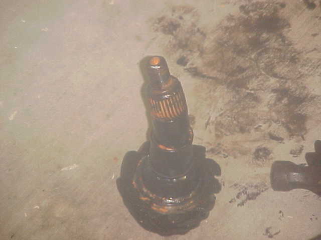 Black automotive part with orange gear teeth, resting on a dirty surface