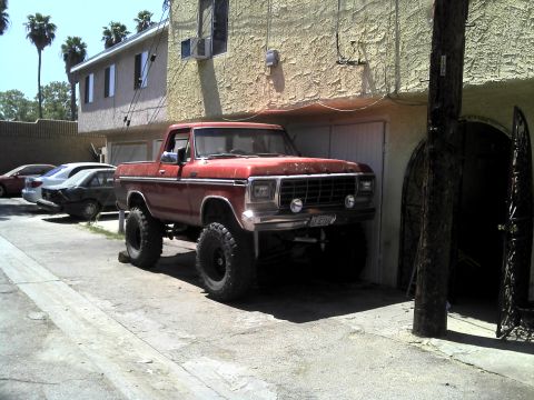 1978 Ford Bronco - This lifted pickup truck has large tires and is parked in front of a building with a garage door.
