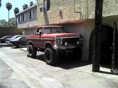 1978 Ford Bronco - A lifted 1978 Ford Bronco pickup truck is parked in front of a building, with other vehicles visible in the background.