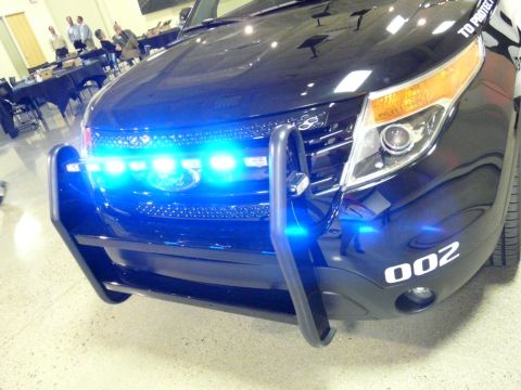 1993 Ford Taurus - Front view of a black police SUV equipped with a push bar and illuminated blue emergency lights. The unit number 002 is visible on the fend…