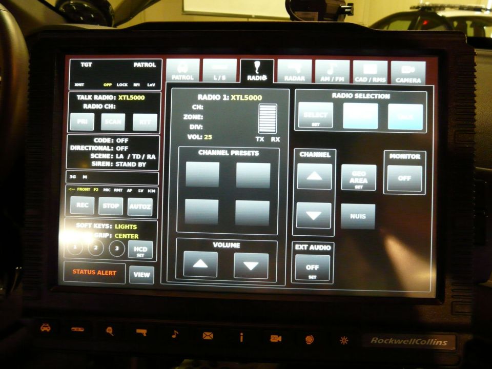 Close-up of a police car's touch screen display showing radio controls, status alerts, and channel presets