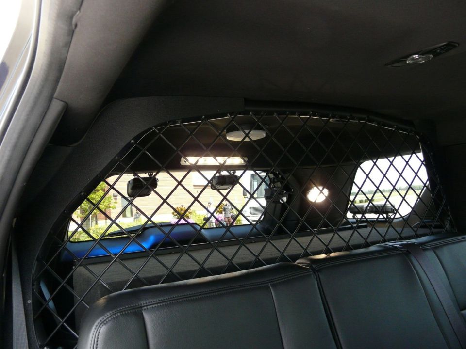 Interior view of a police vehicle showing black leather seats and a metal partition behind the front seats