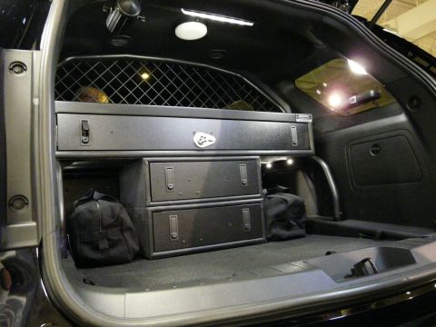 1993 Ford Taurus - The rear cargo area of a police vehicle is outfitted with a partition, multiple storage drawers, and bags.