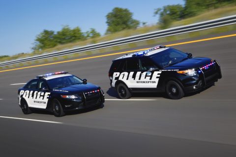 1993 Ford Taurus - Two police interceptor vehicles, a sedan and an SUV, are captured in motion on a highway under a clear blue sky.