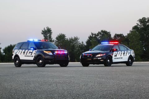 1993 Ford Taurus - Two Ford Police Interceptor vehicles, an SUV and a sedan, are parked on asphalt with their emergency lights activated.