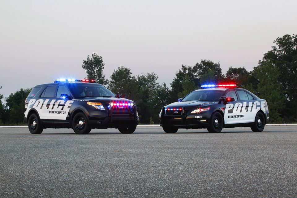 Black and white police SUV and sedan with lights on, parked on asphalt