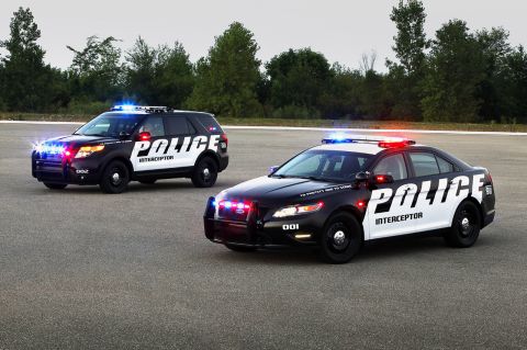 1993 Ford Taurus - Two police interceptor vehicles, an SUV and a sedan, are parked on an asphalt surface with trees in the background.