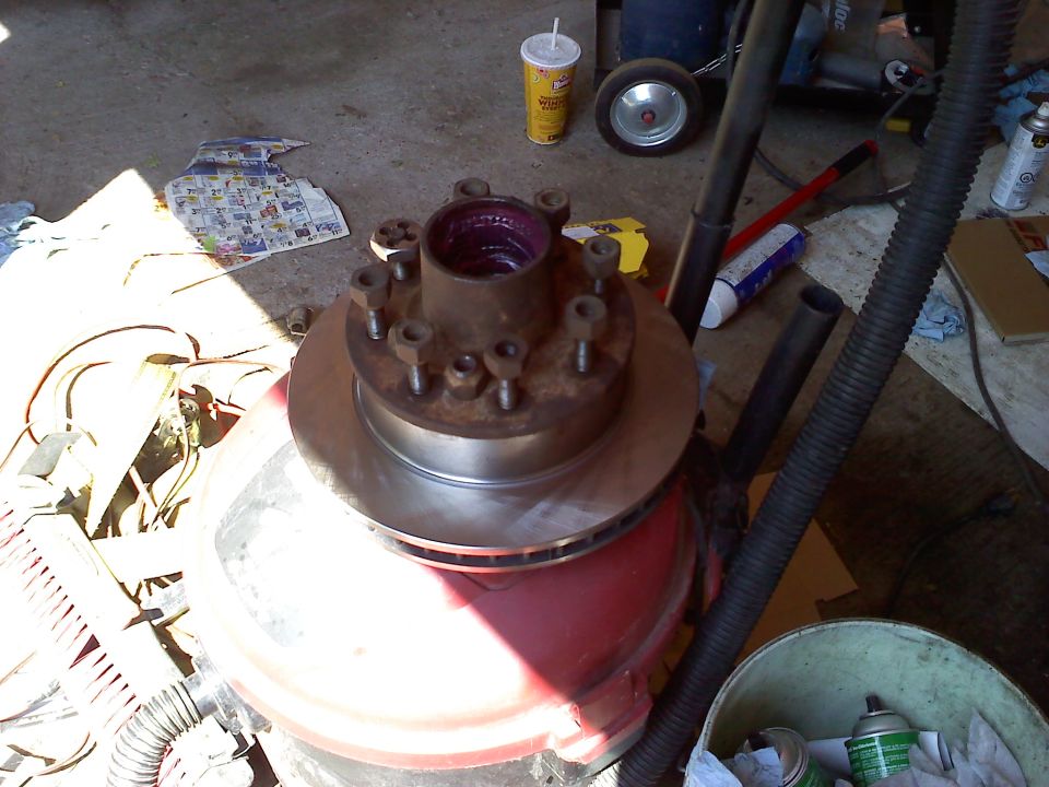 Brake rotor and hub assembly sitting on a red drum in a cluttered garage