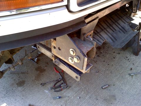 1996 Ford F-150 - Close-up of a front bumper mounting bracket, showing hardware and tools scattered on the ground.