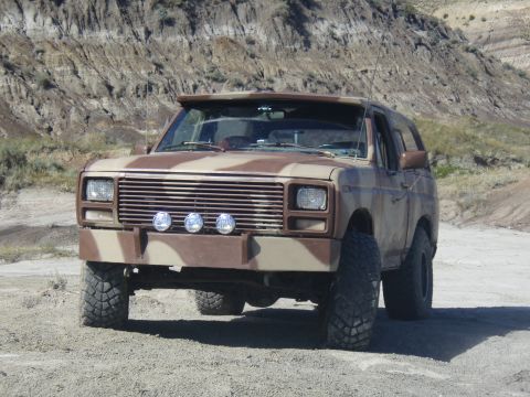 1985 Ford Bronco - A camouflaged Ford Bronco sits on a dirt road with a rocky hillside in the background.