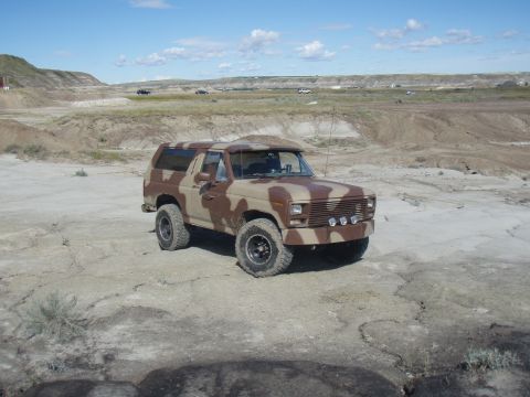 1985 Ford Bronco - This camouflaged SUV, likely from the early 1980s, is parked in a dry, arid landscape.