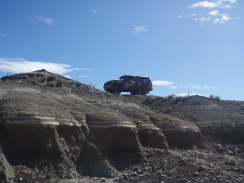 1985 Ford Bronco - A camouflaged SUV navigates a , eroded hillside under a bright, partly cloudy sky.