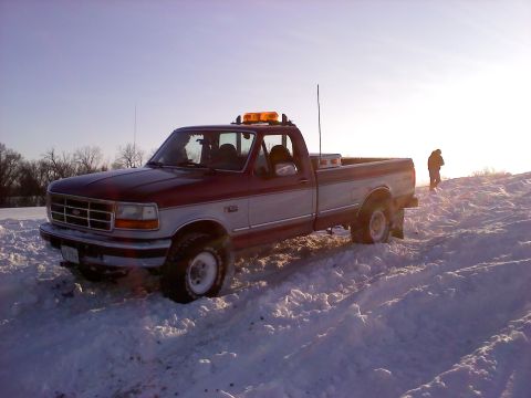 1996 Ford F-150 - A two-tone red and silver 1996 Ford F-150 pickup truck navigates a snowy terrain under a bright sky.