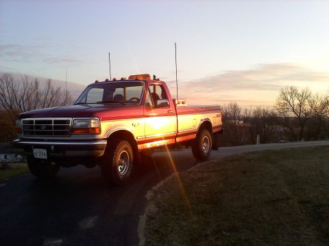 1996 Ford F-150 - A red and white Ford F-250 truck is parked on a paved surface during sunset.
