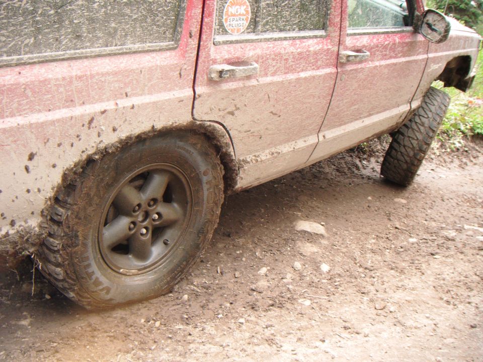 Mud-covered red Jeep Cherokee on a dirt track, front wheel turned