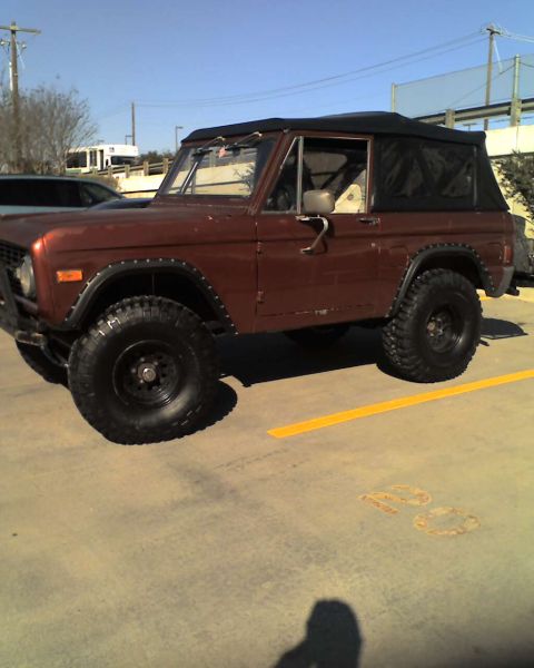 1977 Ford Bronco - A brown 1977 Ford Bronco is shown from a three-quarter front angle, a black soft top and large off-road tires.