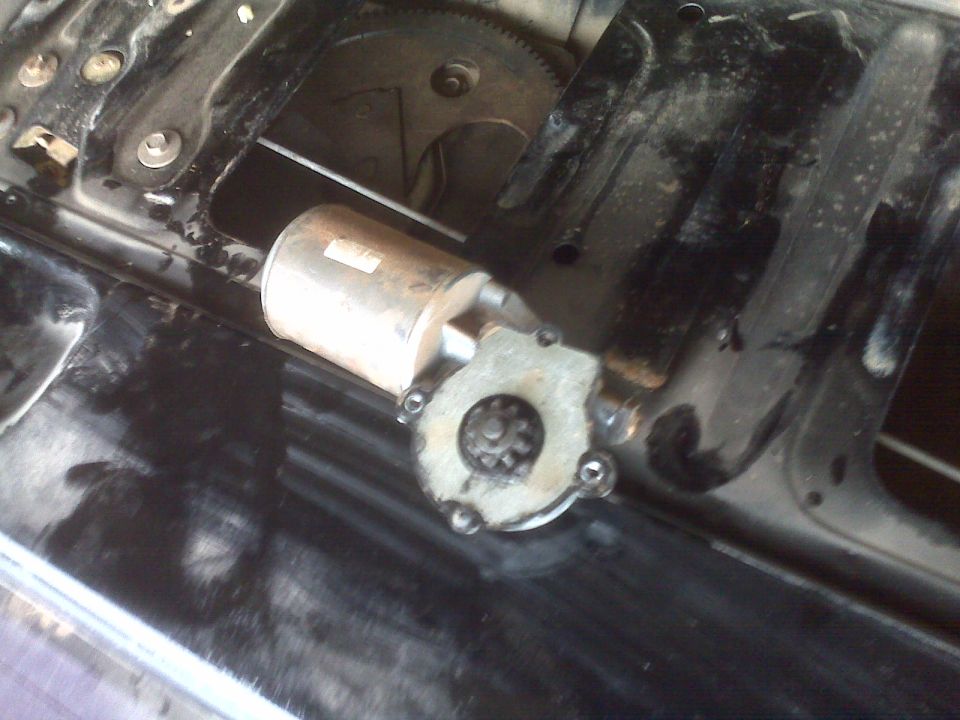 Silver electric window motor with small gear next to black regulator assembly with large gear