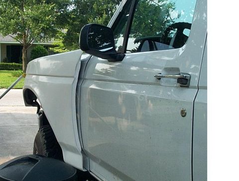 1995 Ford Bronco - Close side view of a white full-size Ford truck's driver's door and front fender in a driveway, showing the chrome door handle, keyed lock…