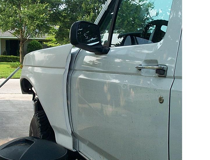 Driver-side door and front fender of a white Ford truck with black tow mirror in a driveway