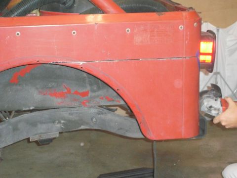 1985 Jeep CJ7 - A person uses an angle grinder on the red body of a Jeep CJ, modifying the rear quarter panel.