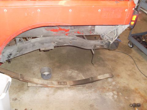 1985 Jeep CJ7 - The rear frame section of an orange Jeep CJ7 is shown with a removed leaf spring and other parts on the garage floor.